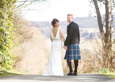 a bride and groom look over their shoulders as they stand outside the cuillin hills hotel at their wedding