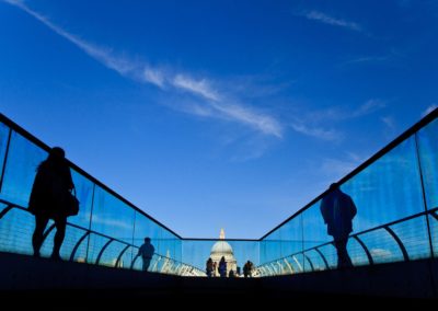 pedestrians are silhoutted by the sky as they walk across the millenium bridge towards st pauls cathedral
