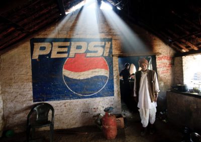 an indian man is lit by a shaft of light next to a pepsi sign