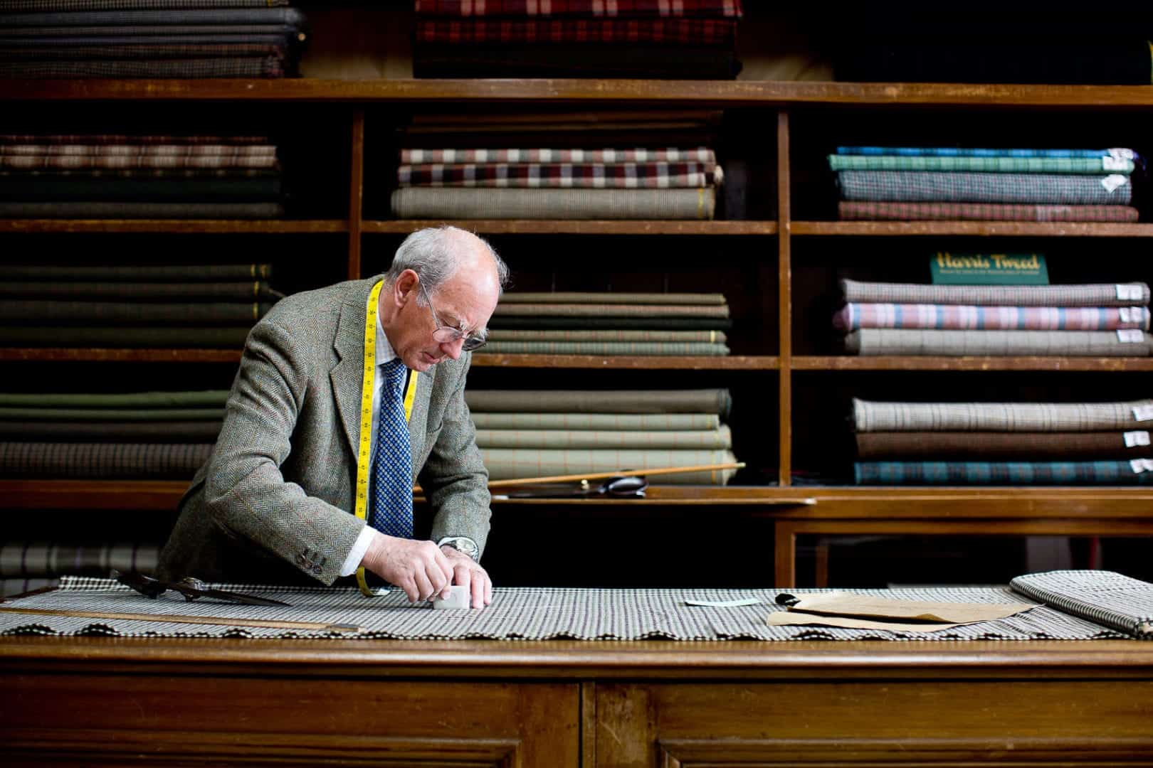 tom, the lead tailor at campbells of beauly tweed shop cuts a length of cloth