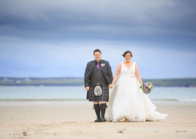 a bride and groom smile for the camera on their wedding day on the isle of lewis