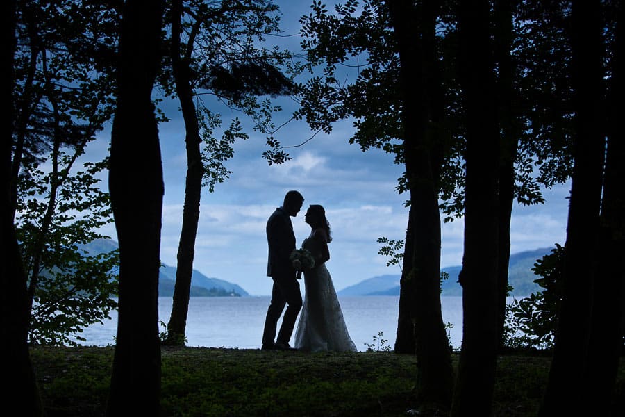 a bride and groom are silhouetted against the sky by loch ness on a pre wedding photo session in scotland